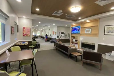Senior center lounge with tables, seating, a fireplace, TV, and artwork.