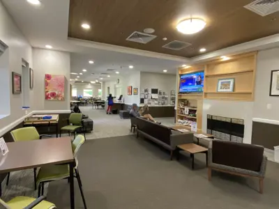 Senior center lounge with tables, seating, a fireplace, TV, and artwork.