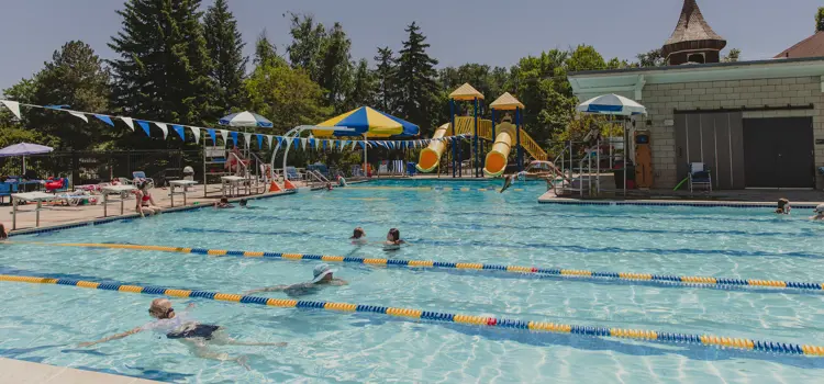 Outdoor swimming pool with lap lanes, zipline, slides. and shaded seating.