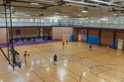 Indoor gymnasium with basketball courts and players.