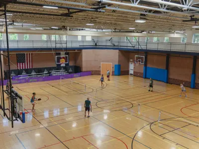 Indoor gymnasium with basketball courts and players.