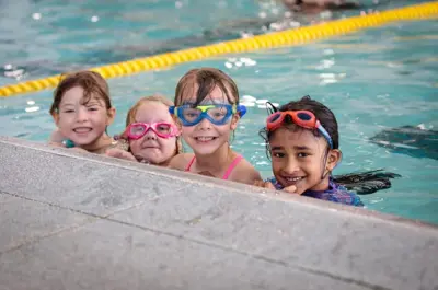 Four children smiling at the edge of an indoor pool.