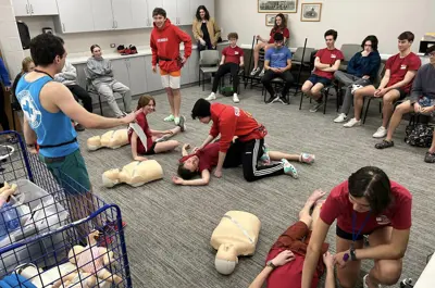 Instructor demonstrating CPR to a seated training group.