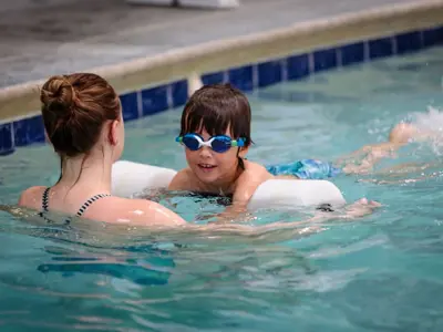 Adult helping a child practice swimming in an indoor pool.