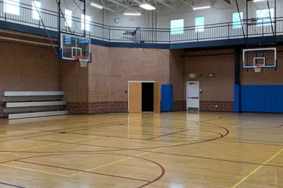 Indoor gymnasium with basketball hoops, bleachers, and court markings