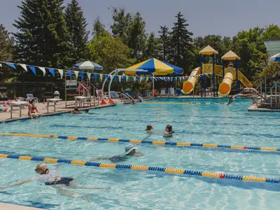 Outdoor swimming pool with lap lanes, zipline, slides. and shaded seating.