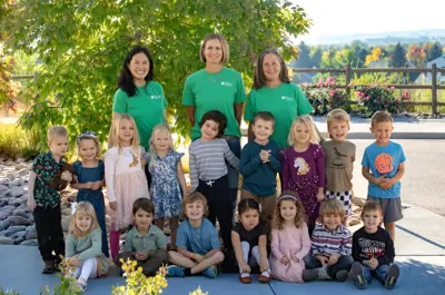 Preschool staff and children pose together outdoors.