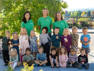Preschool staff and children pose together outdoors.