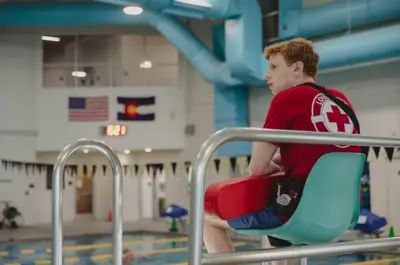 Lifeguard seated beside an indoor pool.