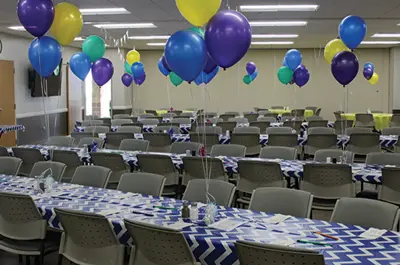 Event room decorated with colorful balloons and patterned tablecloths.
