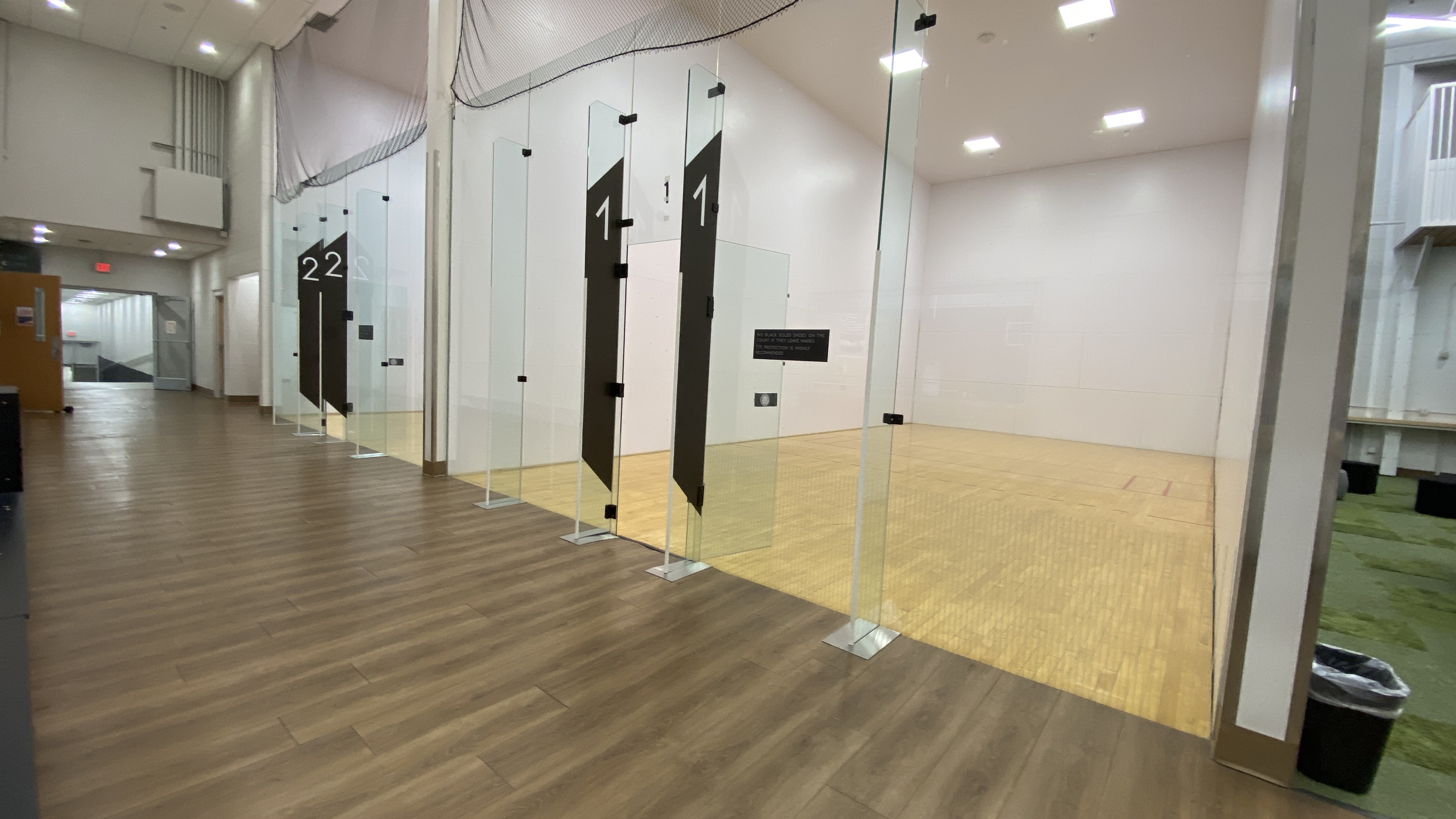 Glass-walled indoor racquetball courts with numbered entrances.